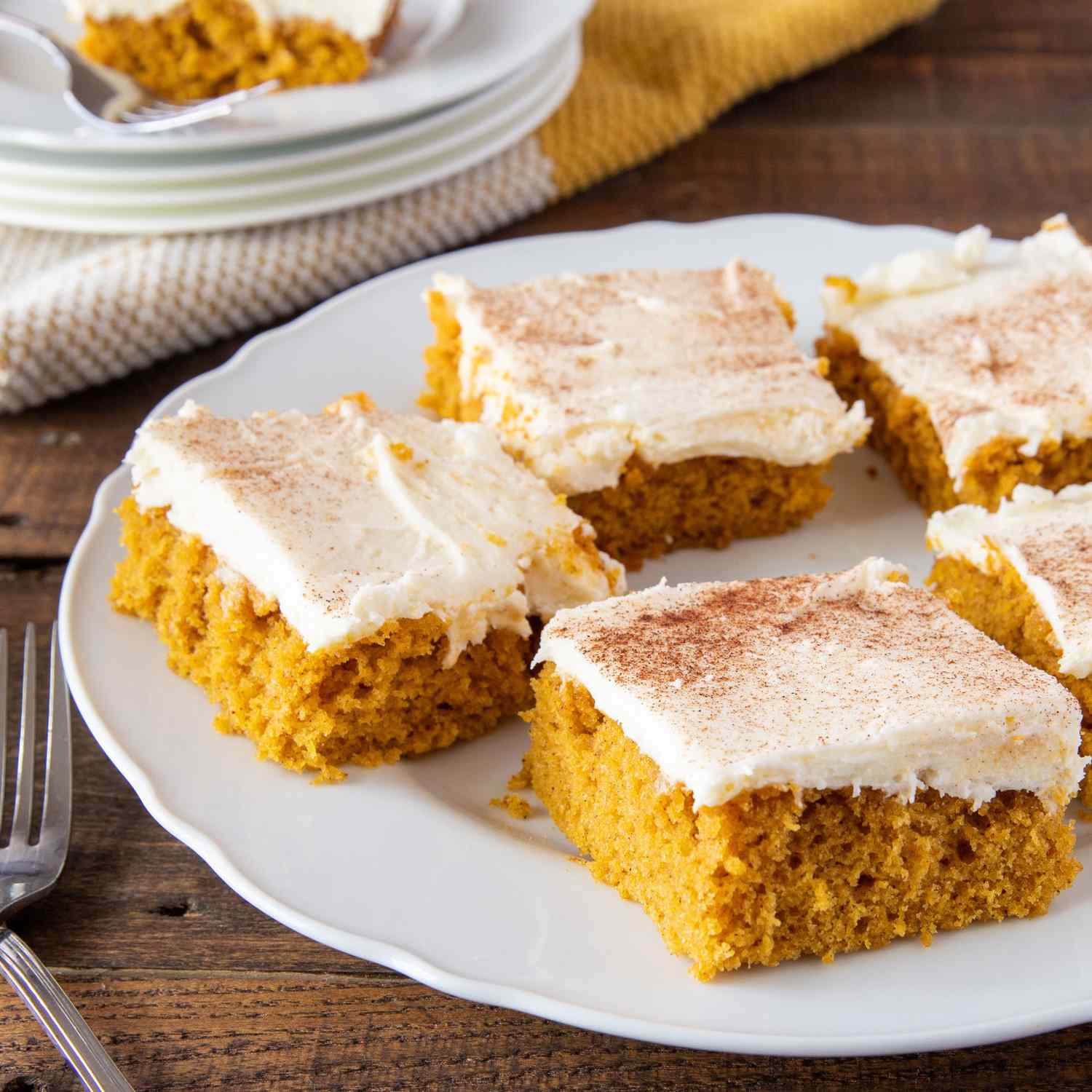 close up on a plate full of pumpkin bars topped with cream cheese frosting