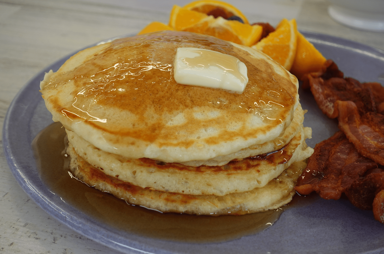 buttermilk pancakes with fruit, bacon, and a pat of butter