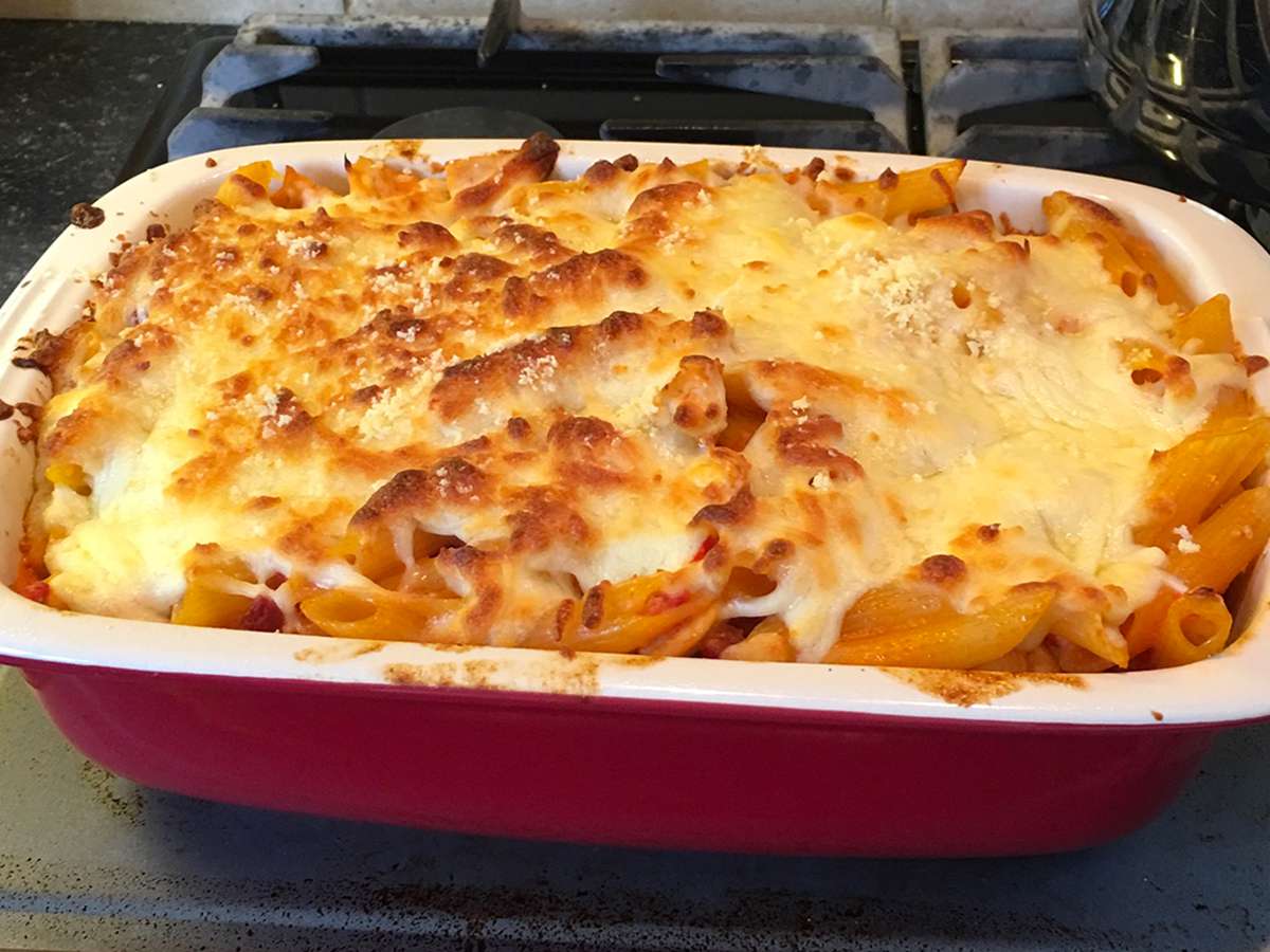 close up view of Chicken and Chorizo Pasta Bake in a white and red baking dish on a stove