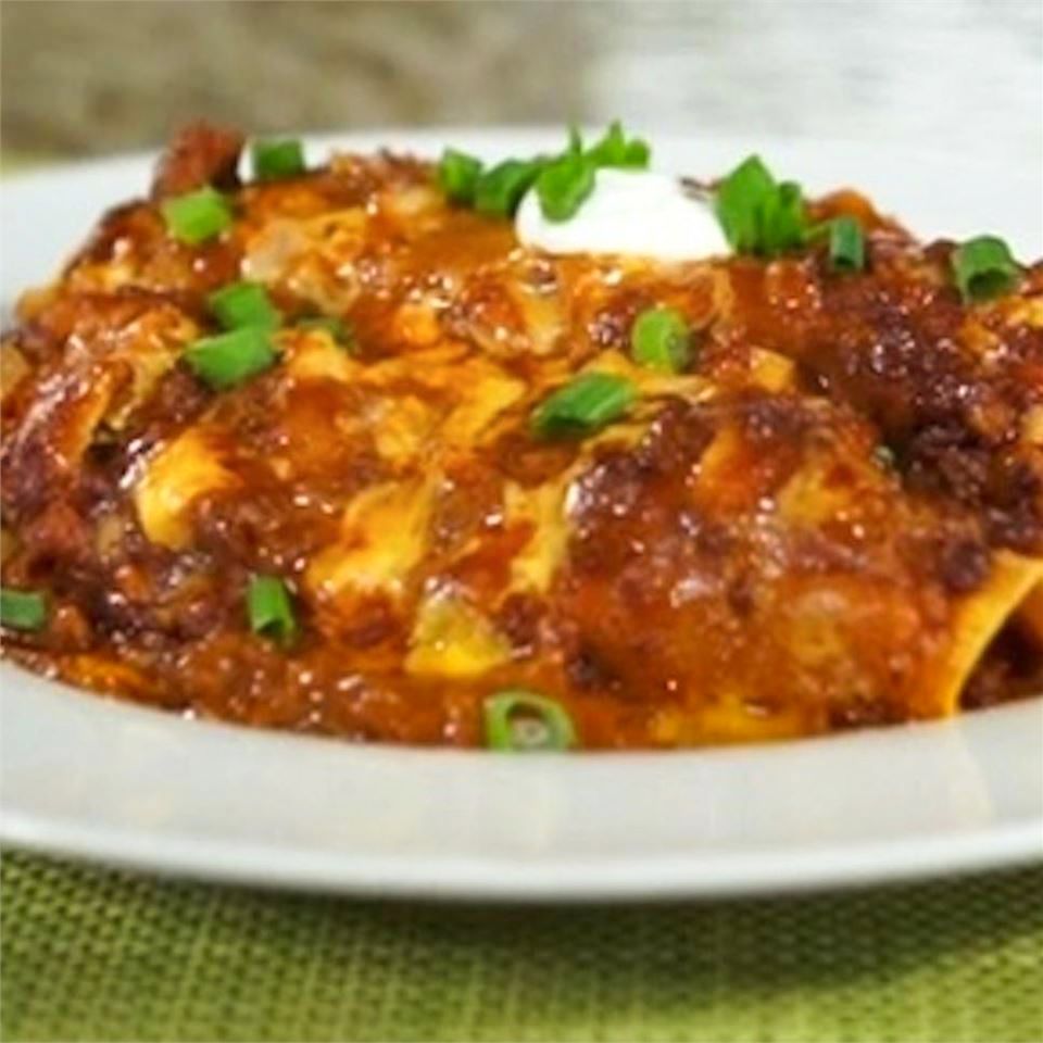 close up view of Cheesy Chili Enchiladas garnished with sour cream and green onions on a white plate