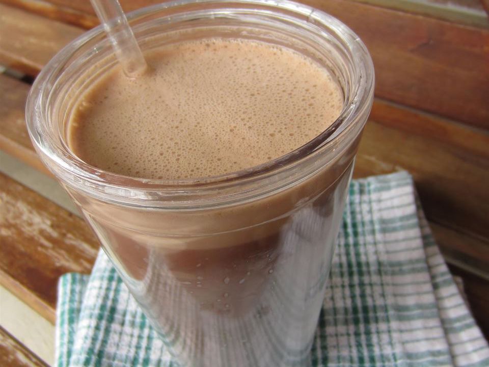 close up view of a chocolate iced mocha in a plastic glass with a straw, on a plaid kitchen towel