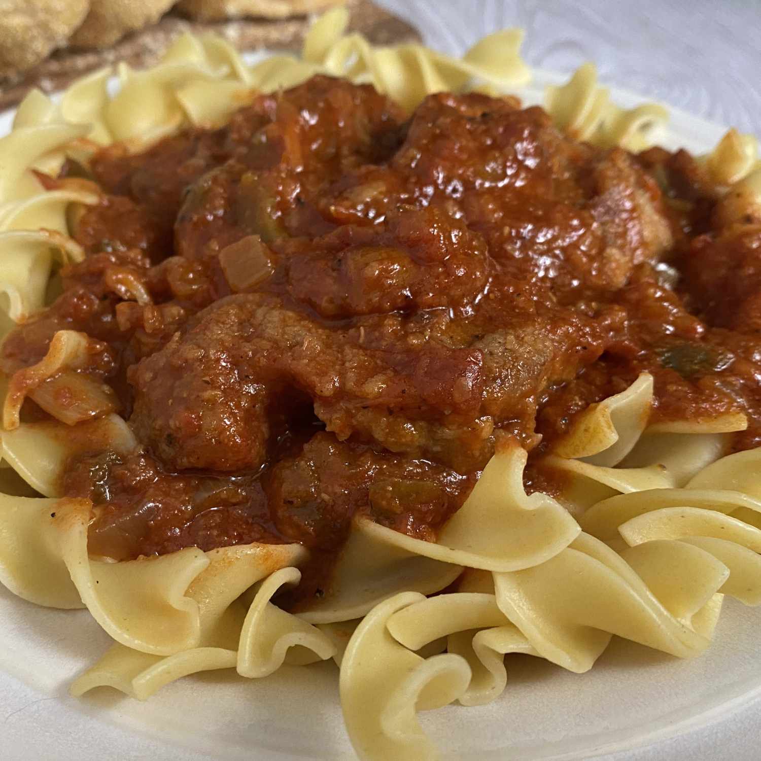 a plate in of beef cubes in tomato sauce served over egg noodles