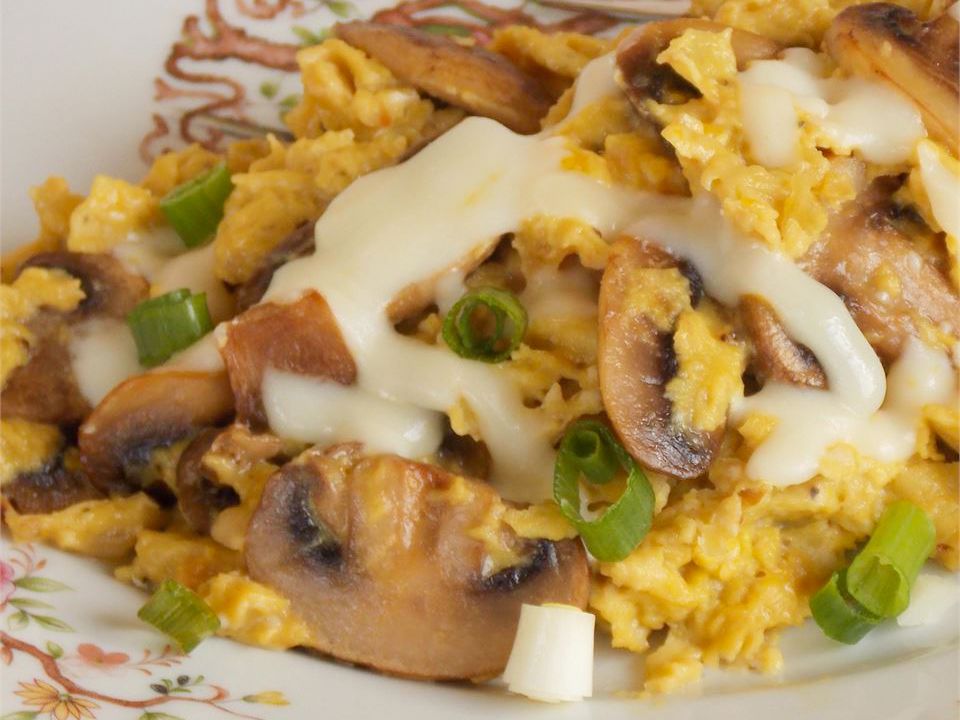 close up view of Onion and Mushroom Scrambled Eggs with cheese and green onions on a plate