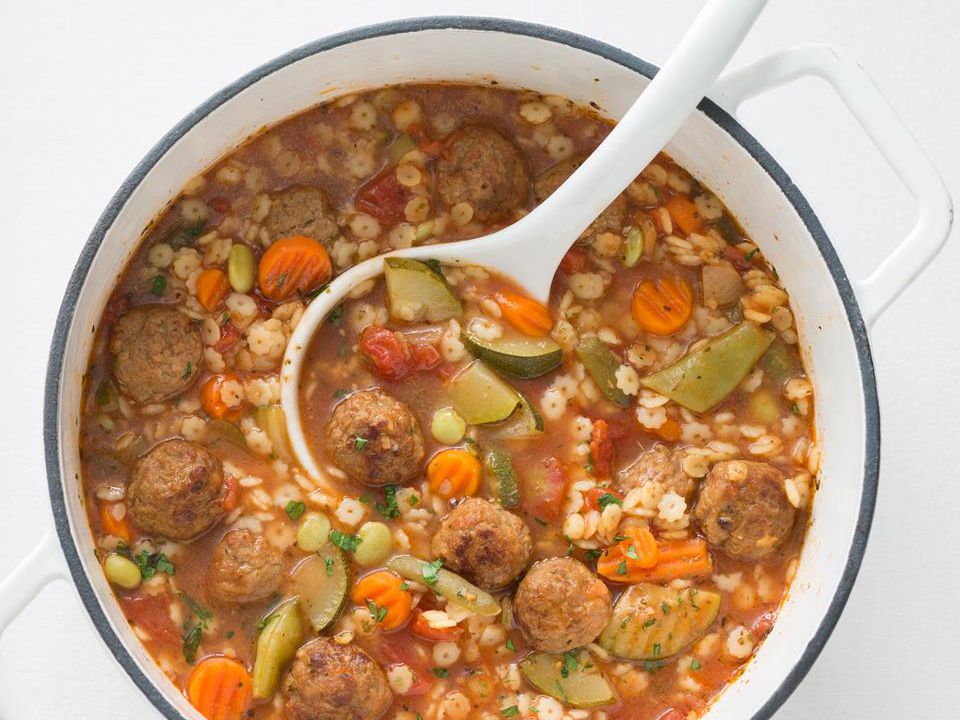 close up view of Hearty Italian Meatball Soup in a white pot with a white ladle