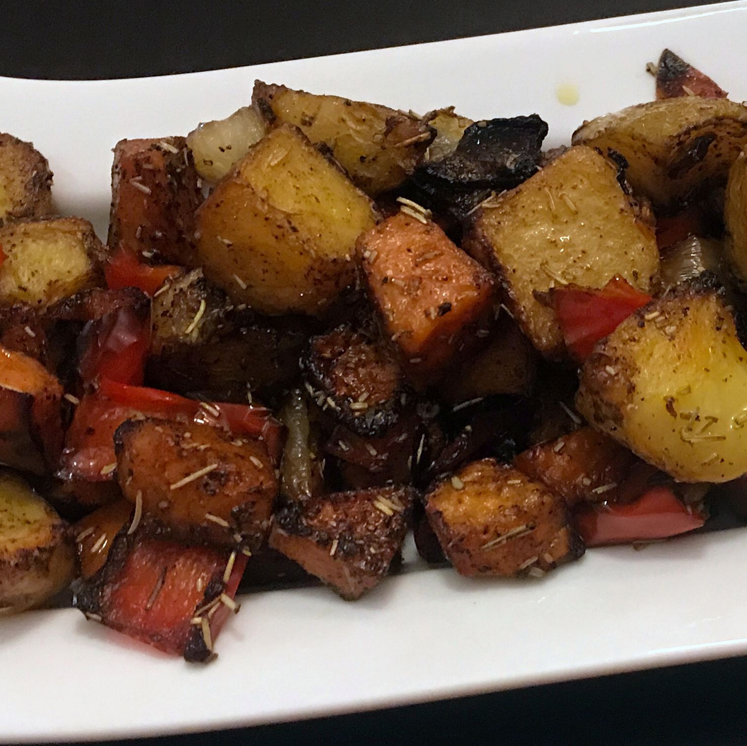 roasted potatoes, carrots, and bell peppers on a white ceramic serving dish