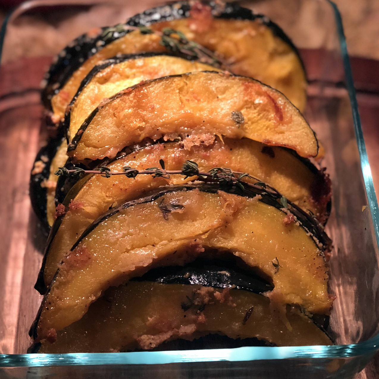 wedges of deep orange roasted squash in a glass baking dish garnished with a thyme sprig