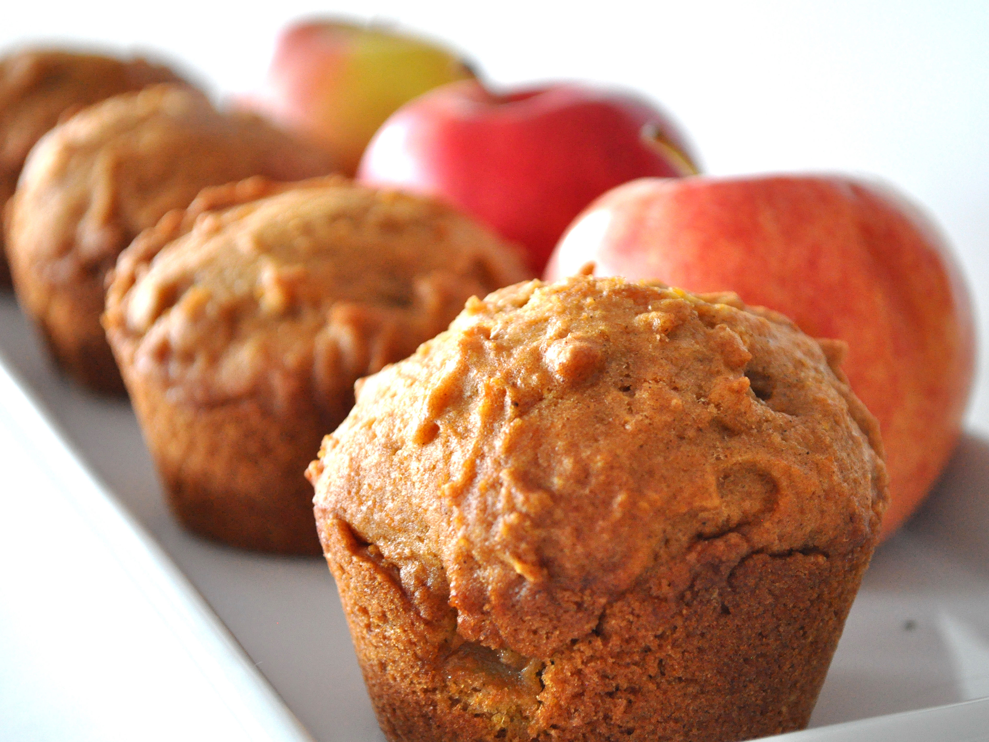 close up view of Pumpkin Apple Streusel Muffins and apples on a white platter