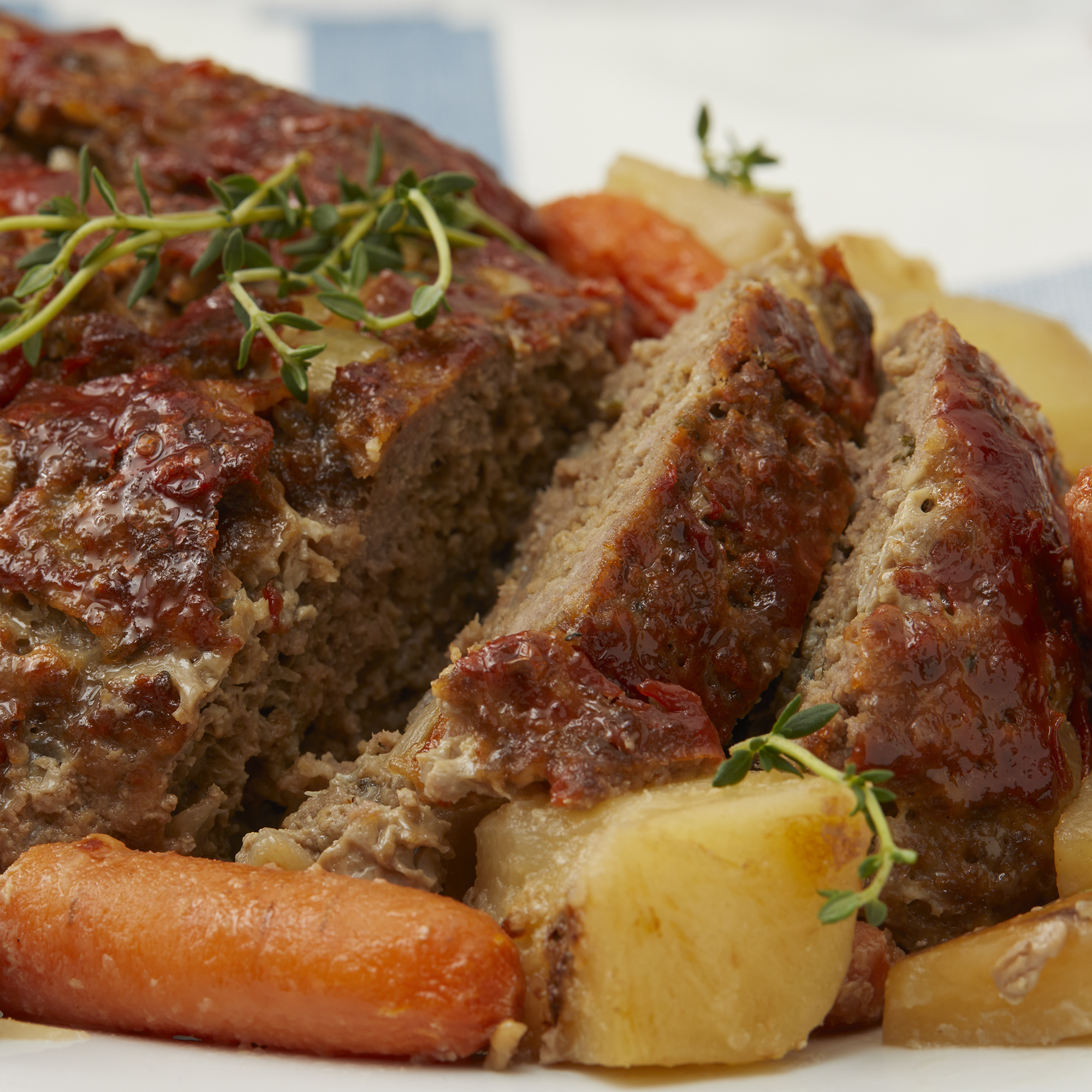 mid angle looking at a platter of slow cooker meatloaf, sliced, with some potatoes and carrots around it