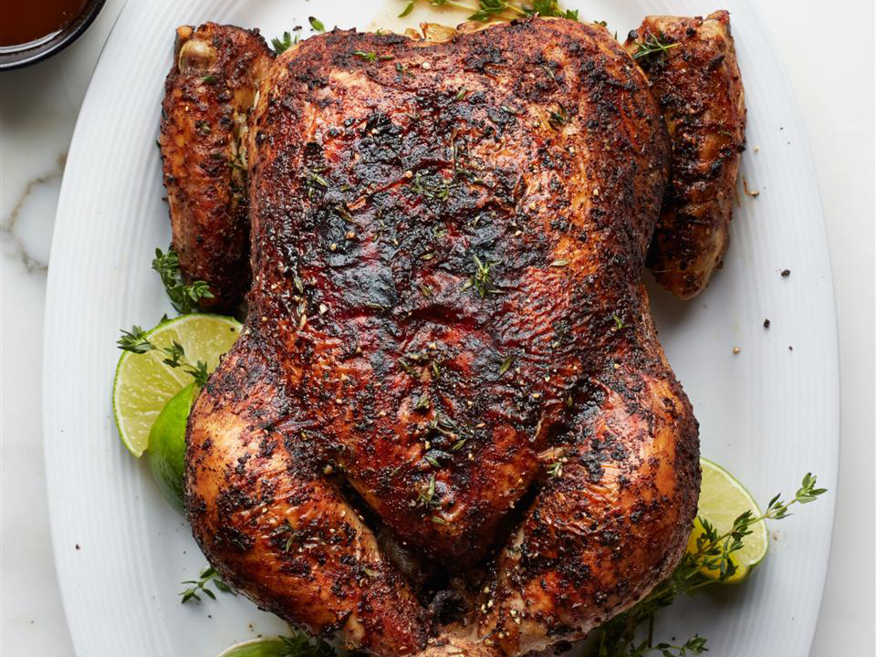 close up view of Caribbean-Spiced Roast Chicken garnished with fresh herbs and lime wedges on a platter