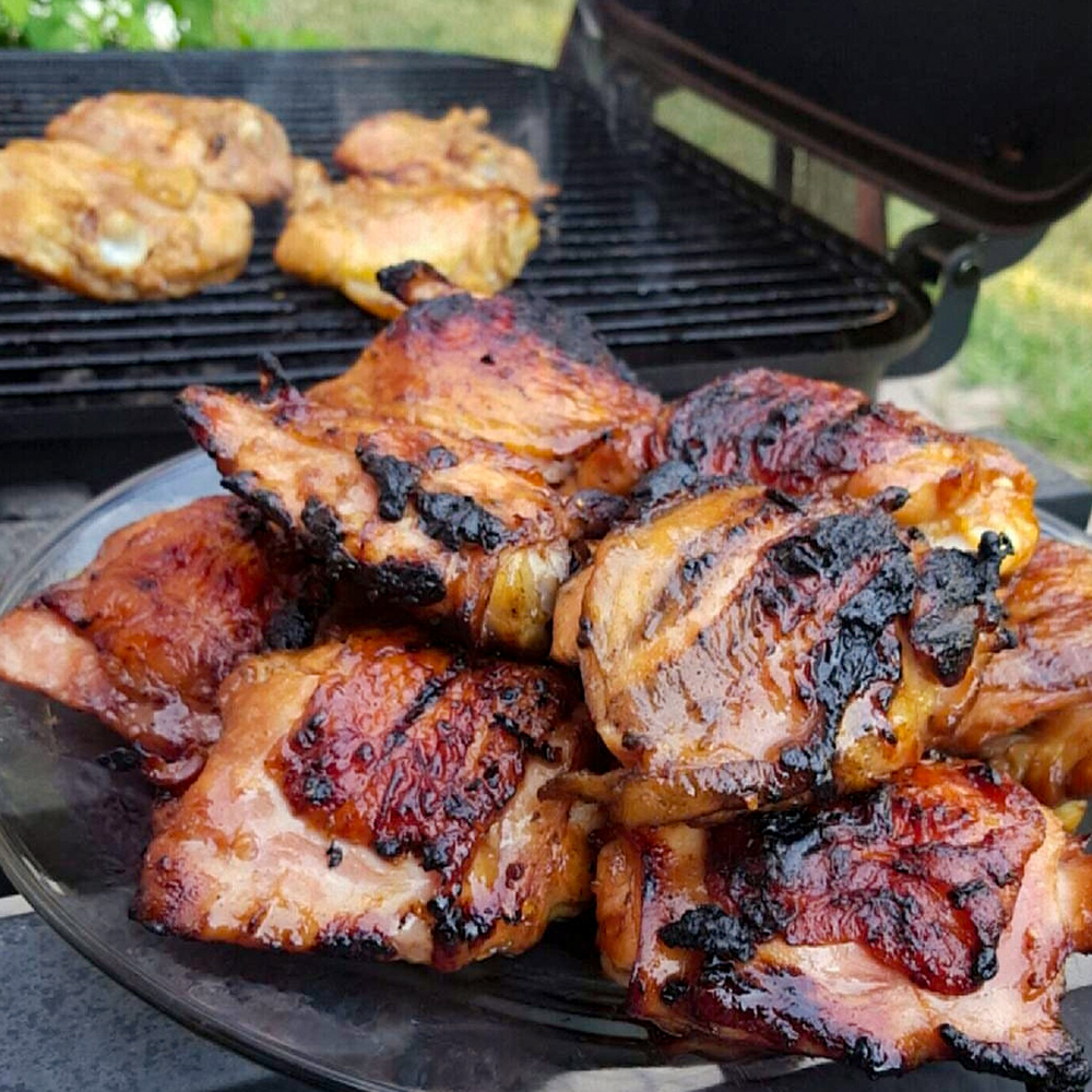 close up view of Asian Grilled Chicken on a platter, with chicken on the grill in the background