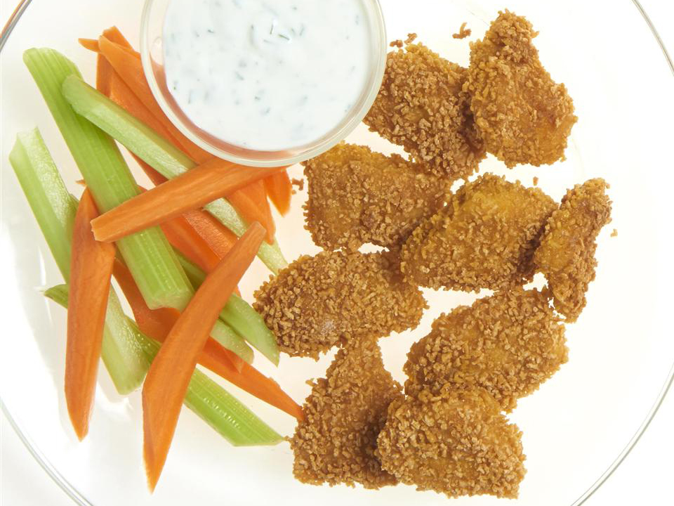 close up view of Chicken Nuggets served with carrots, celery, and white sauce in a glass bowl