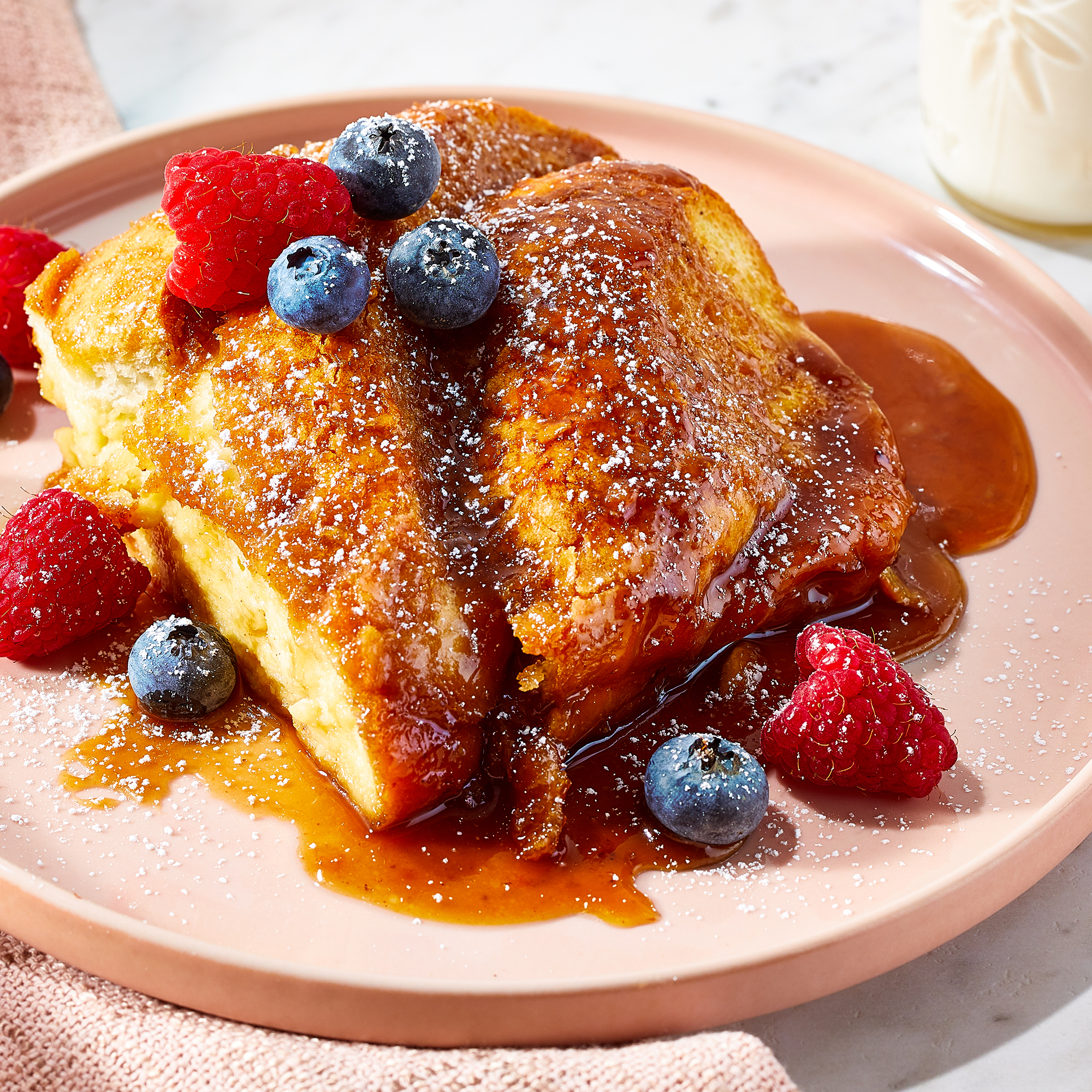 high angle looking at a plate with two slices of baked french toast, topped with syrup and fresh fruit