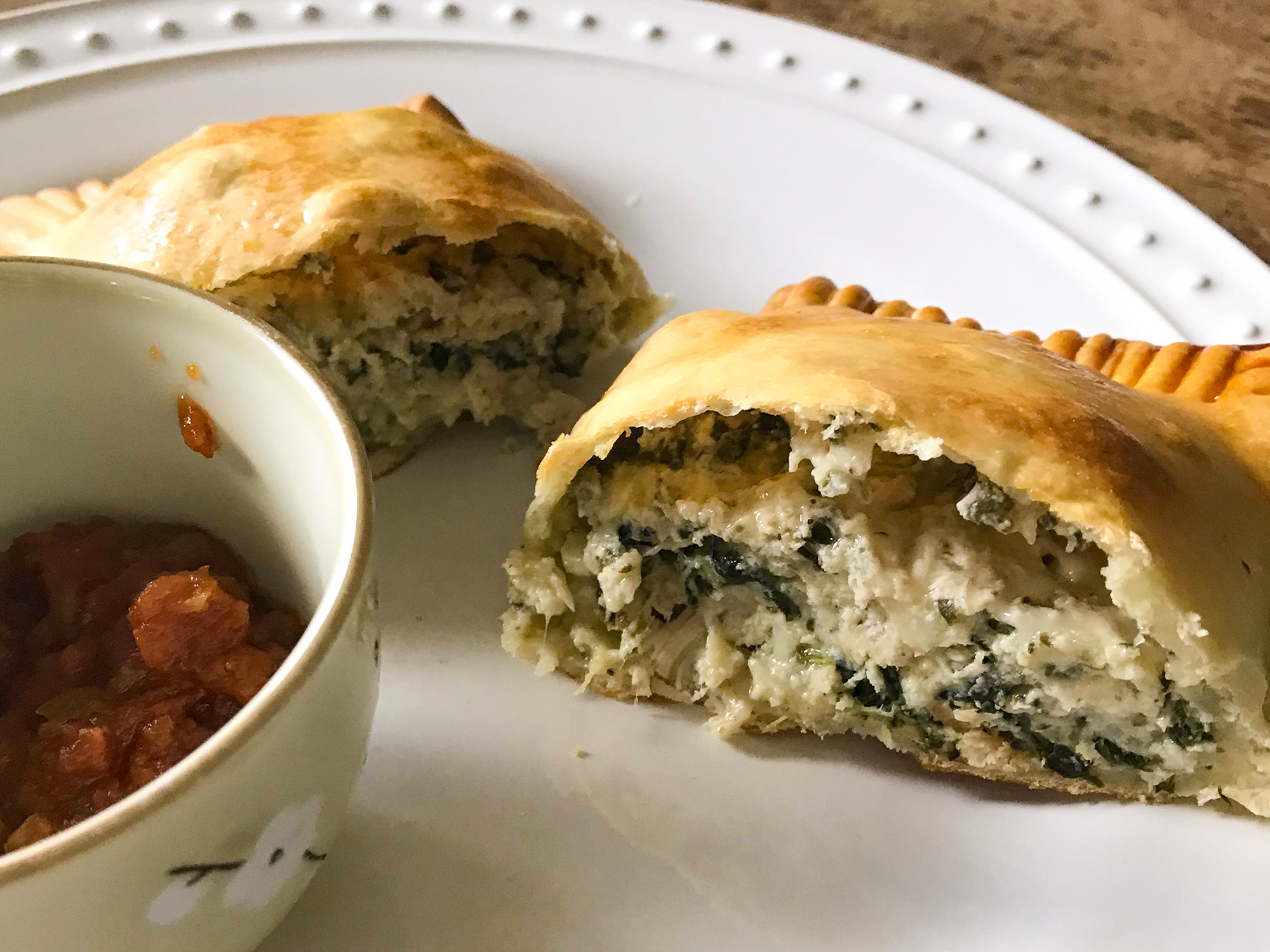 close up view of a sliced Spinach Calzone served with red sauce in a sauce bowl on a plate