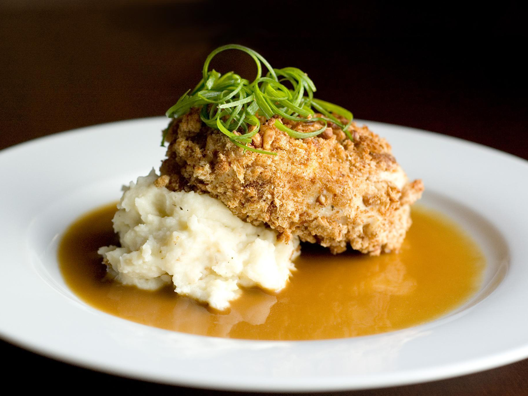 close up view of Bourbon Pecan Chicken served with mashed potatoes and gravy, garnished with green onions on a white plate