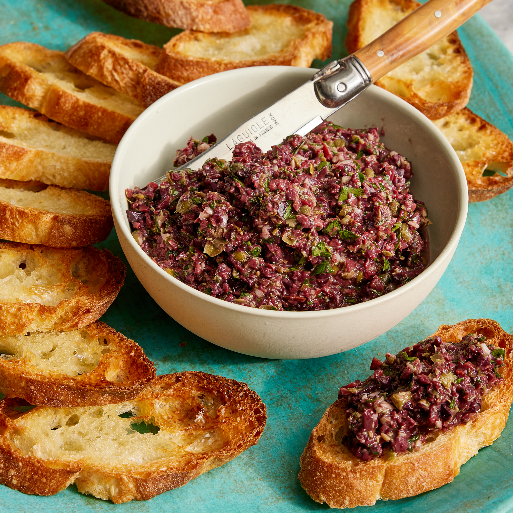 looking at a bowl of kalamata olive tapenade with a side of toasted and sliced baguettes