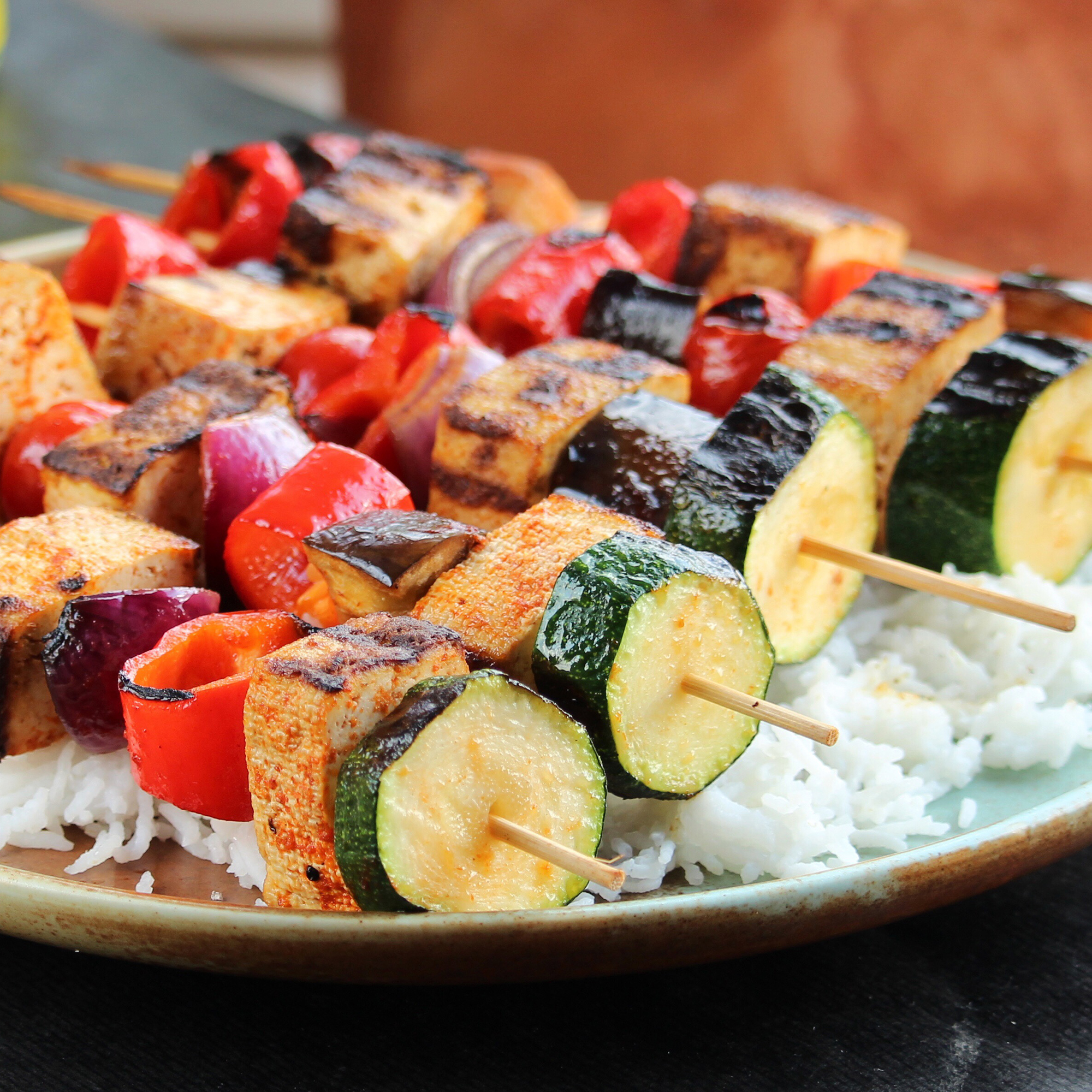 close up view of Grilled Tofu Skewers with Sriracha Sauce and vegetables over white rice on a platter