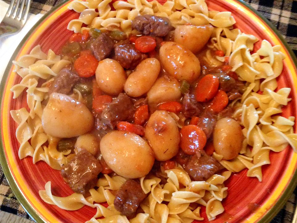 close up view of Beef Stew over noodles on a red plate