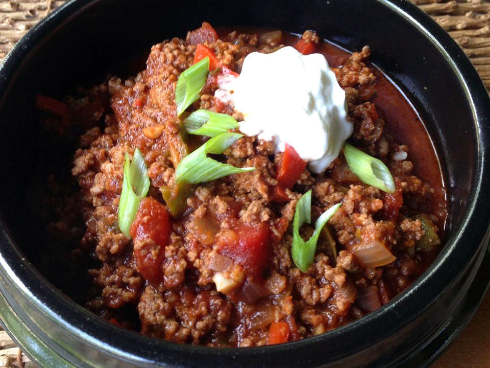 close up view of Paleo Chili garnished with sour cream and green onions in a black bowl