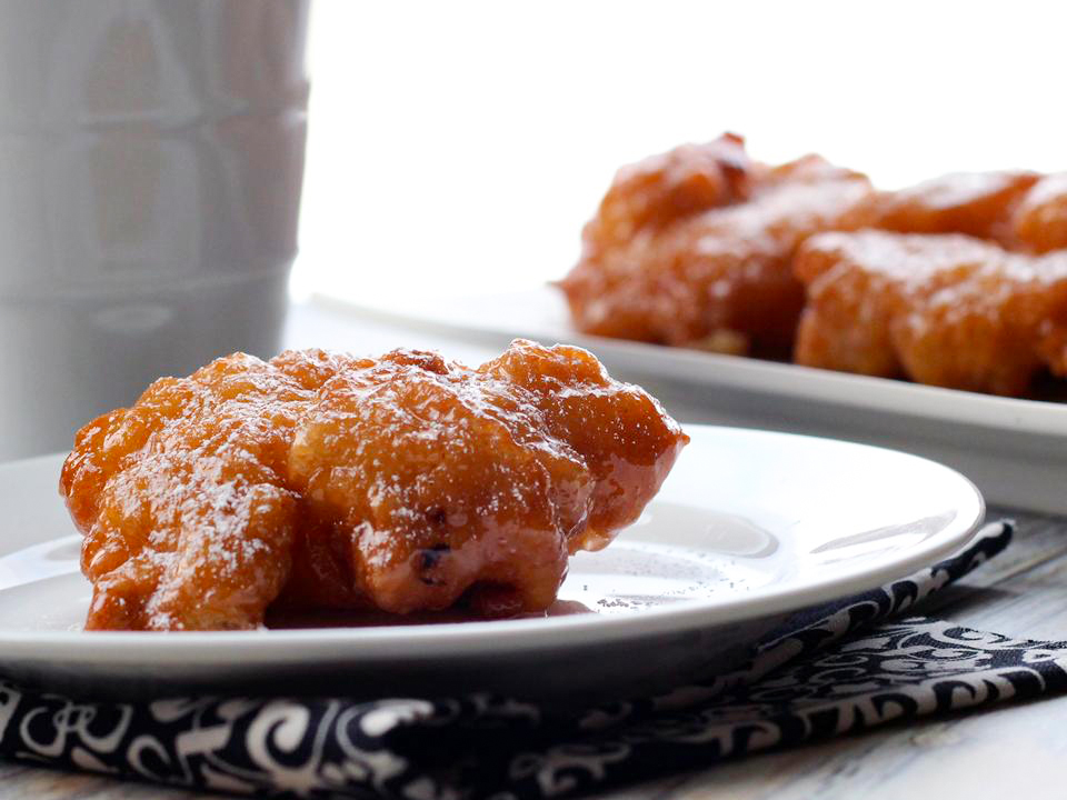 close up view of a Pineapple Fritter on a white plate and Pineapple Fritters on a white platter in the background