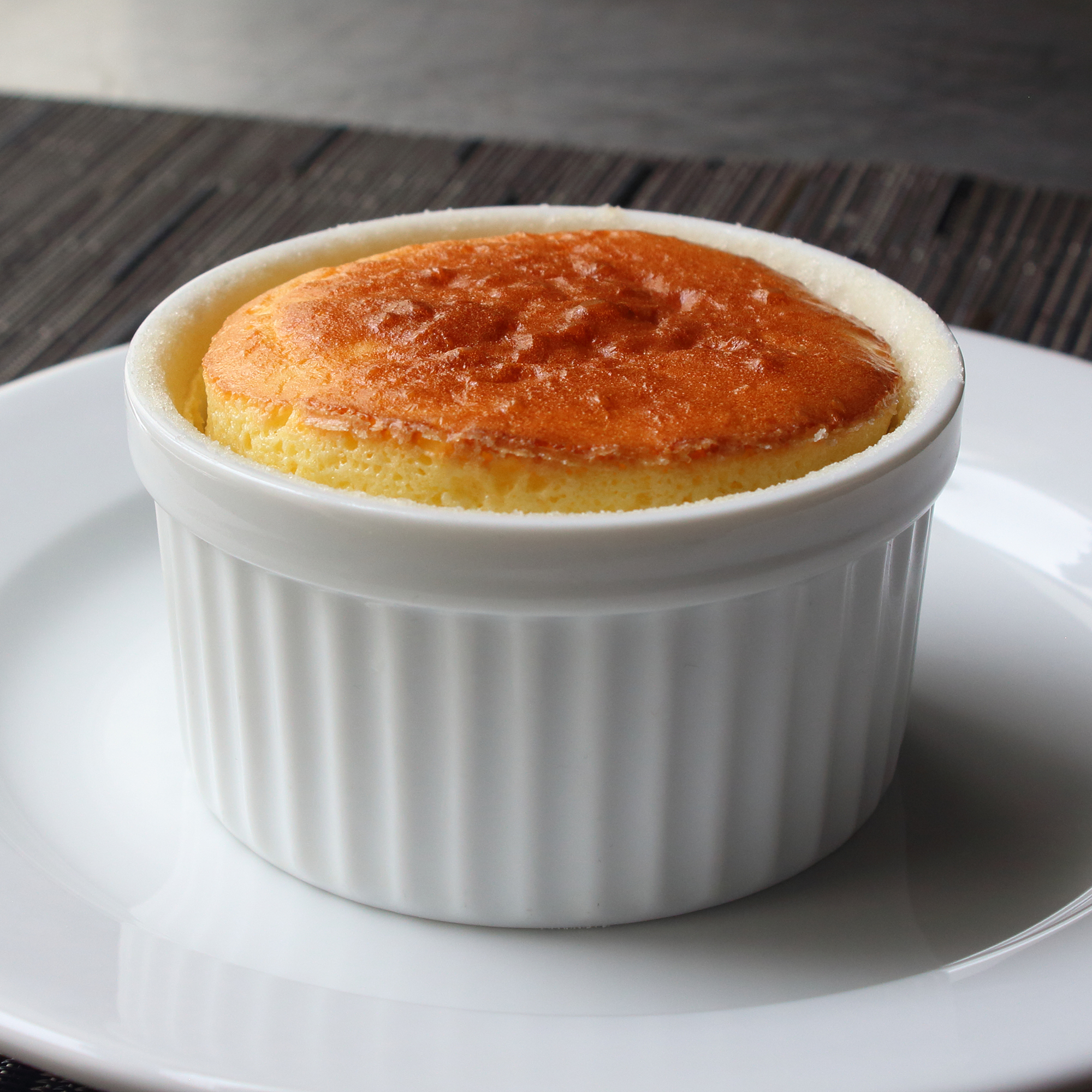 close up view of a Cheese Souffle in a white ramekin on a white plate