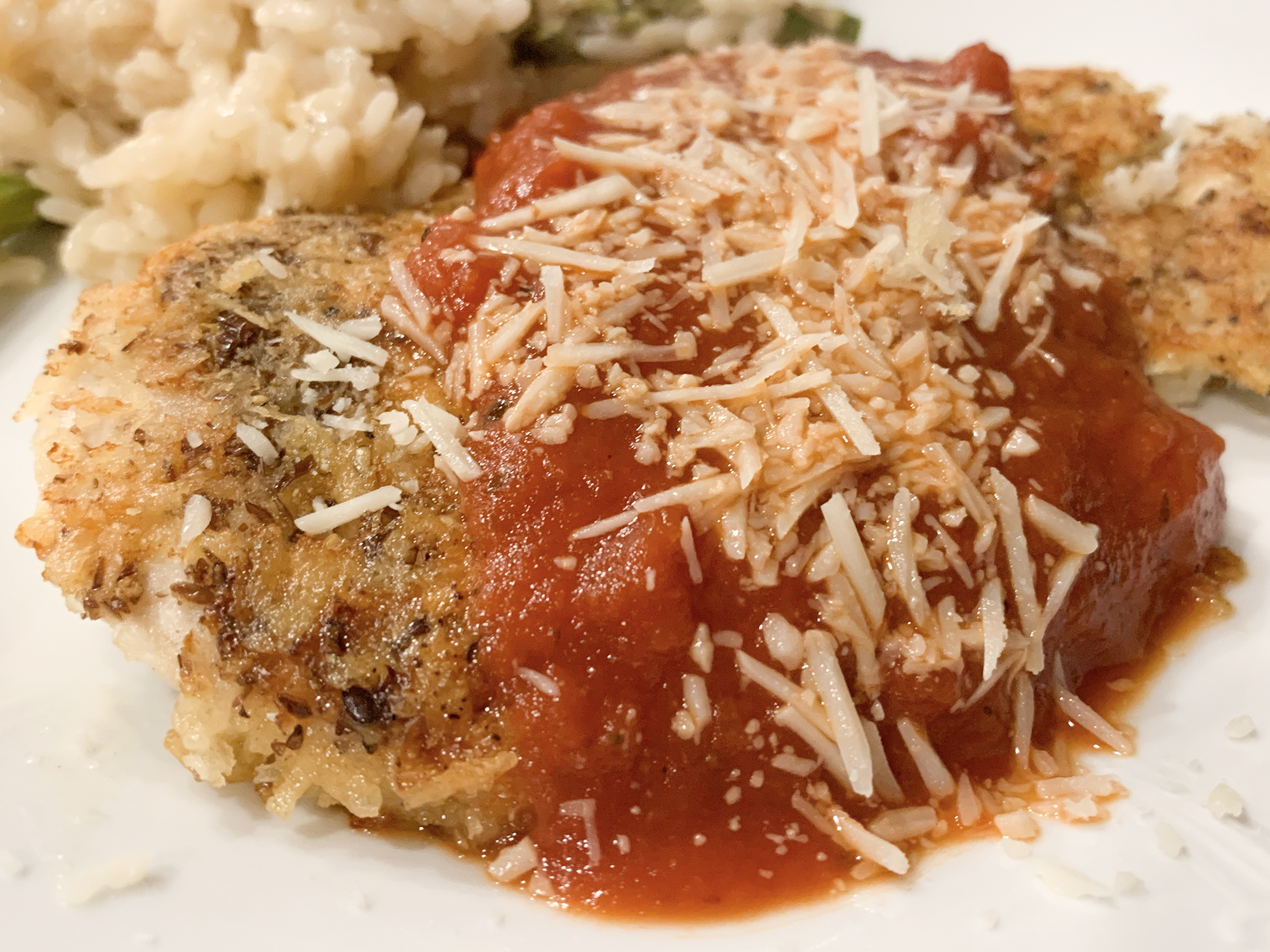 close up view of Homemade Chicken Parmigiana garnished with red sauce and cheese, served with rice on a plate