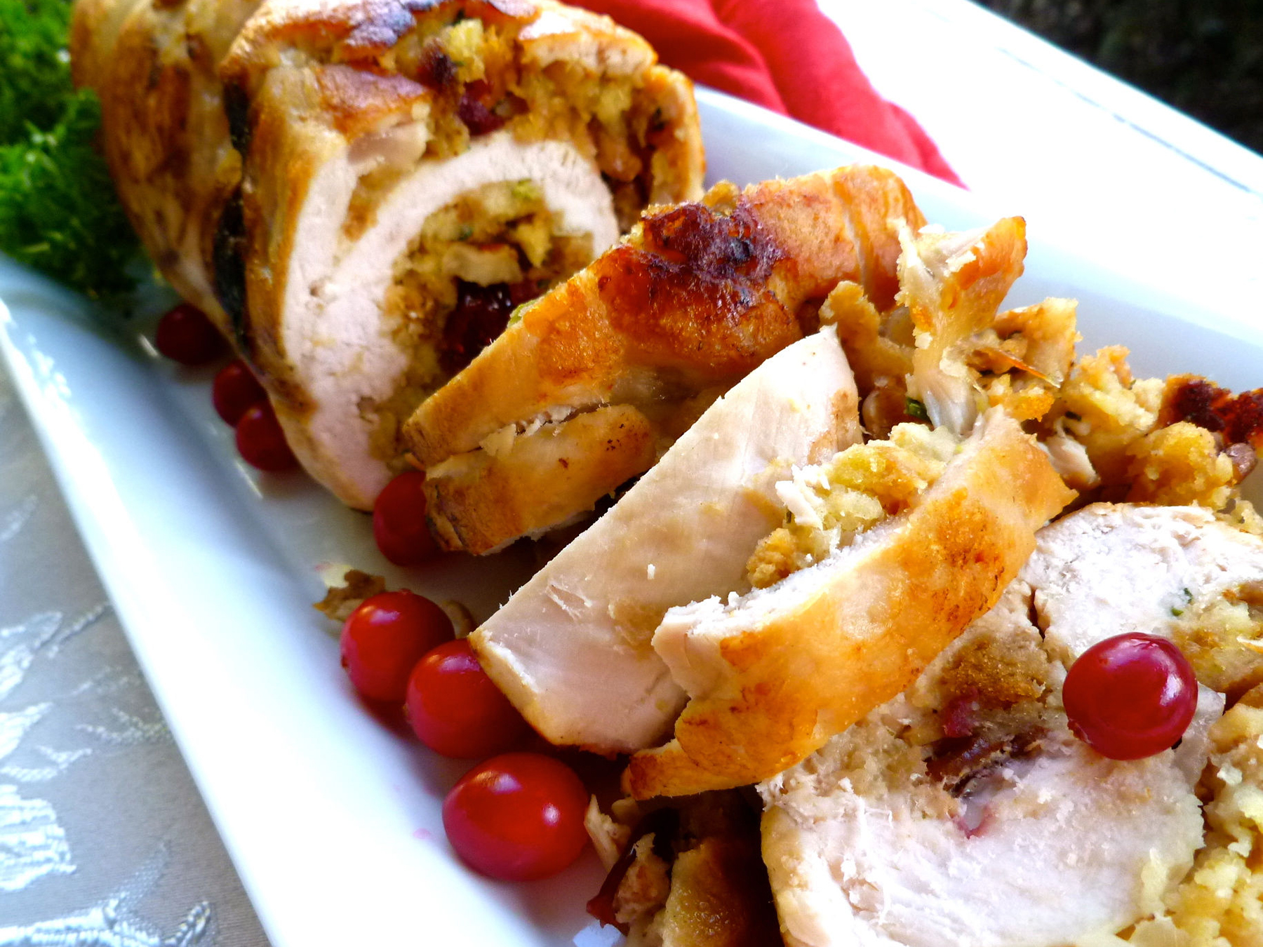 close up view of a sliced Cranberry Stuffed Turkey Breast roll garnished with fresh cranberries on a white platter