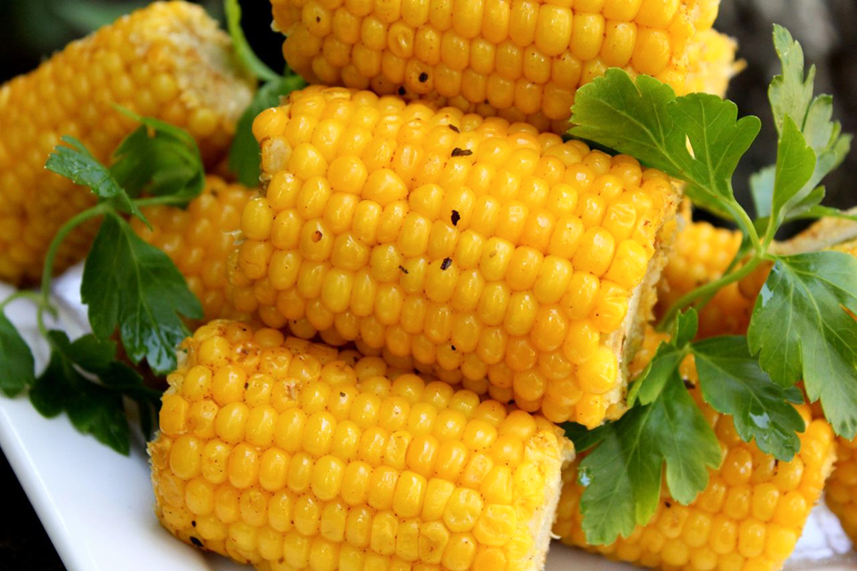 close up view of a pile of cobs of corn garnished with fresh herbs on a white plate