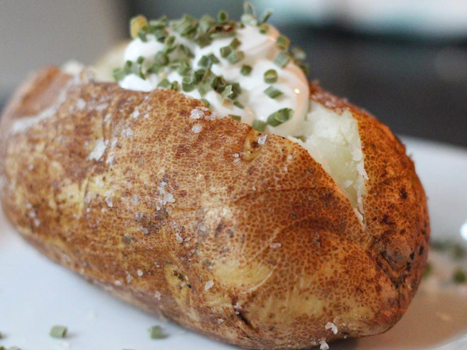 close up view of a Garlic Baked Potato garnished with sour cream and green onions on a white plate