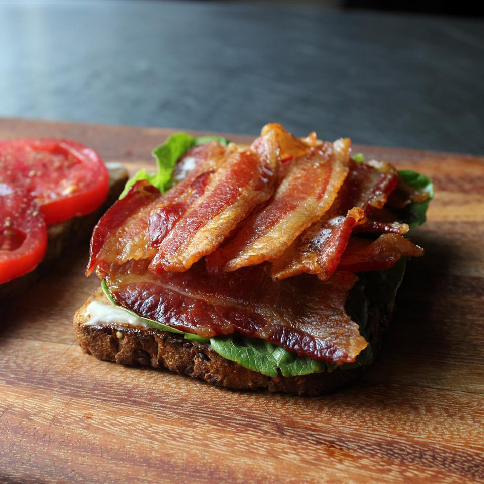 close up view of a bacon, lettuce and tomato sandwich on a wooden cutting board