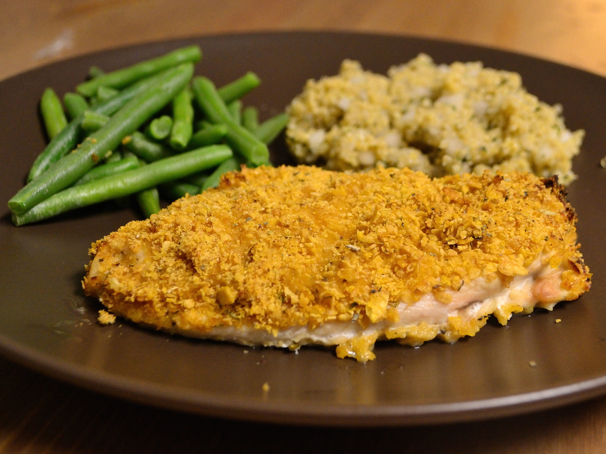 close up view of a fillet of breaded chicken served with green beans and rice on a plate