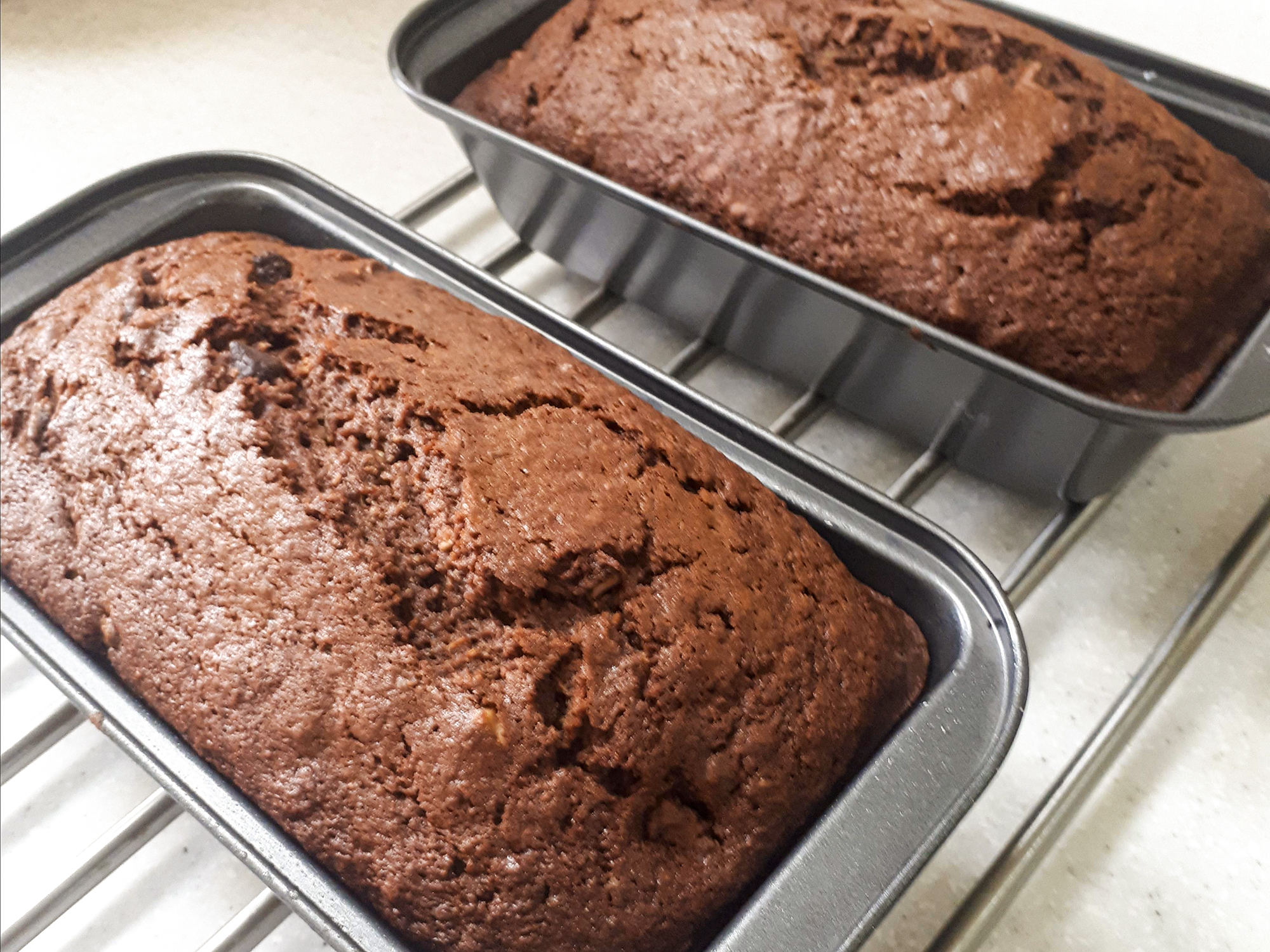 close up view of Chocolate Zucchini Bread in loaf pans on a cooling rack