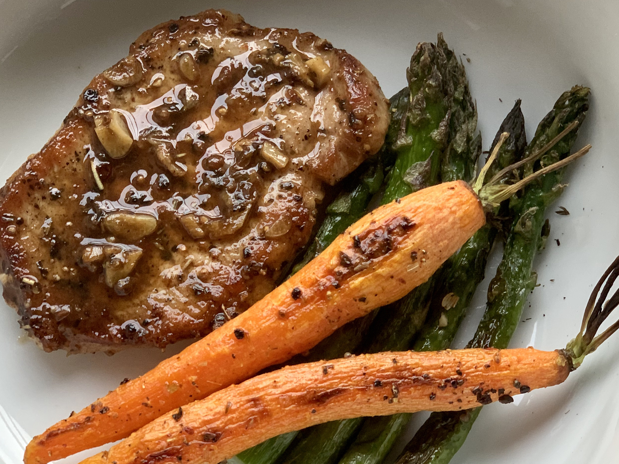 close up view of a Modenese Pork Chop served with carrots and asparagus in a white bowl
