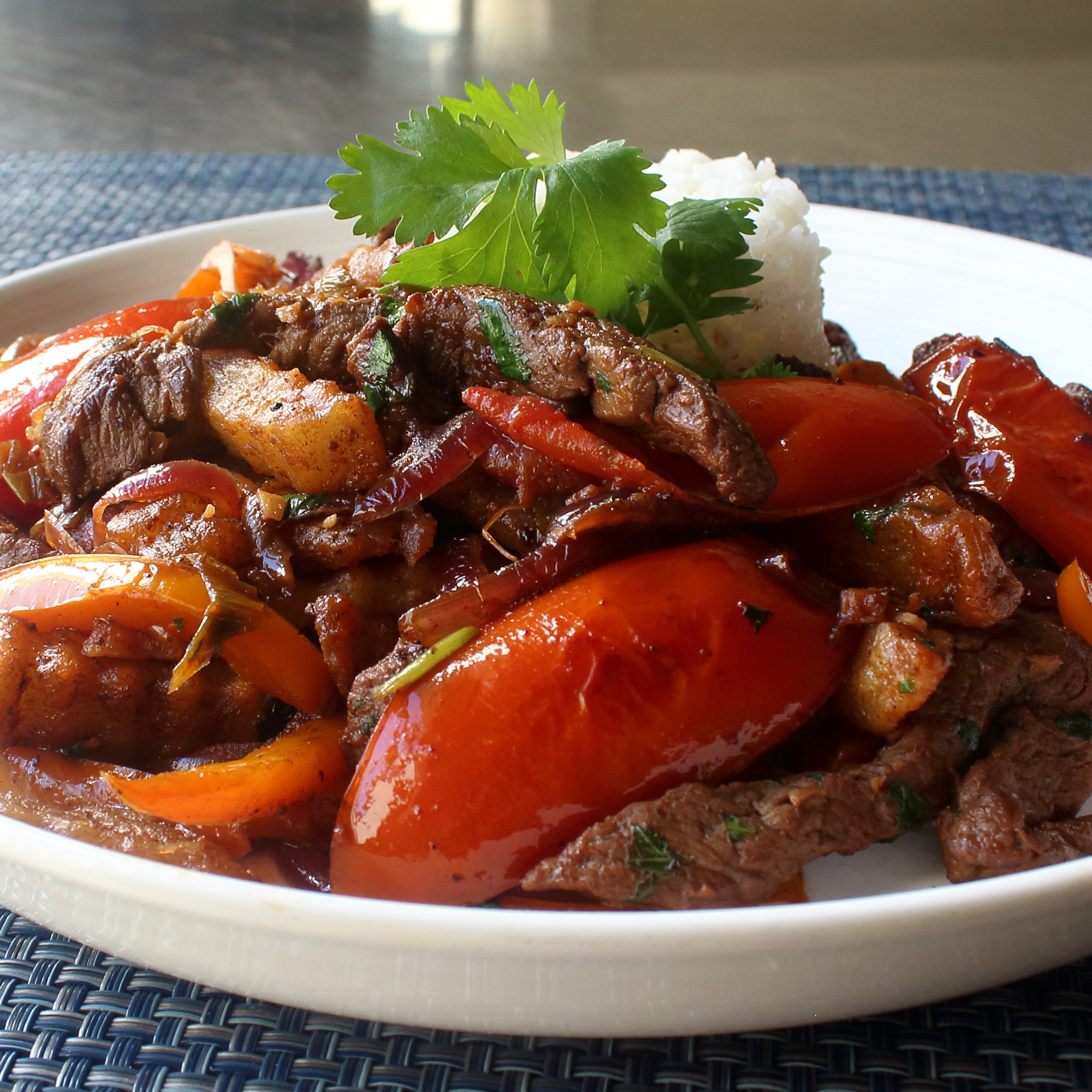 close up view of Lomo Saltado (Peruvian Steak Stir-Fry) with white rice and fresh herbs on a white plate