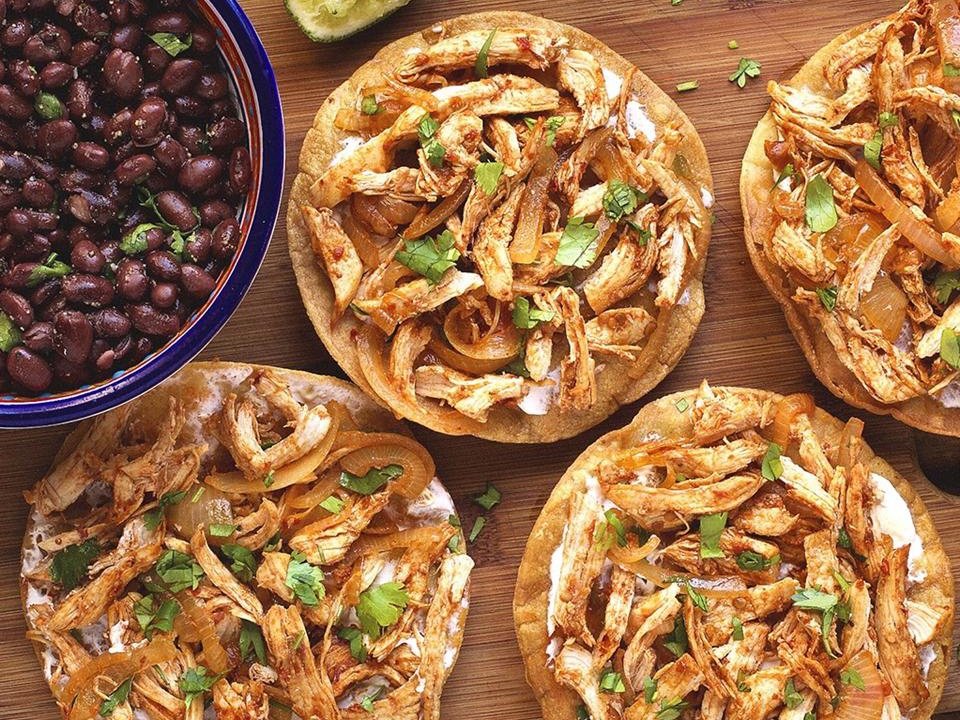 close up view of Chicken Tinga Tostados garnished with fresh herbs, served with black beans in a bowl