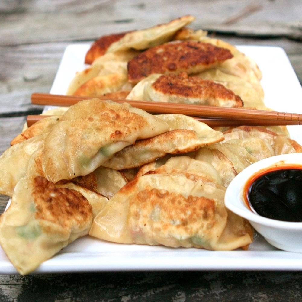 close up view of Potstickers (Chinese Dumplings) with dipping sauce and chopsticks on a white platter
