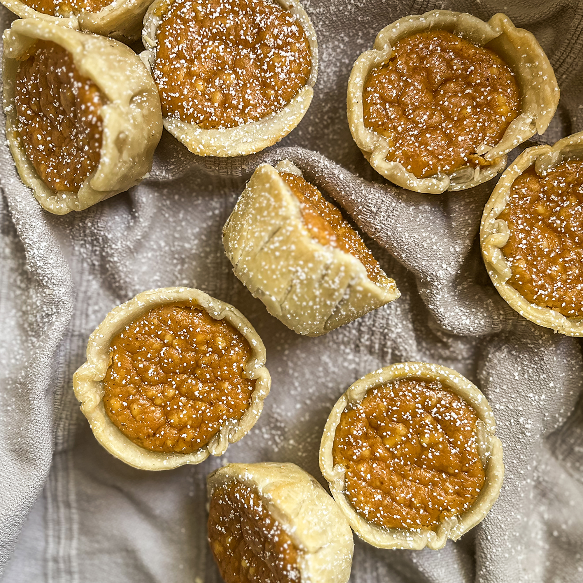 a top down view of several mini pumpkin pies dusted in powdered sugar cooling on a towel