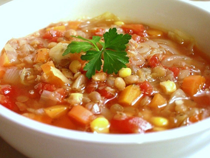 close up view of Winter Lentil Vegetable Soup garnished with fresh herbs in a white bowl