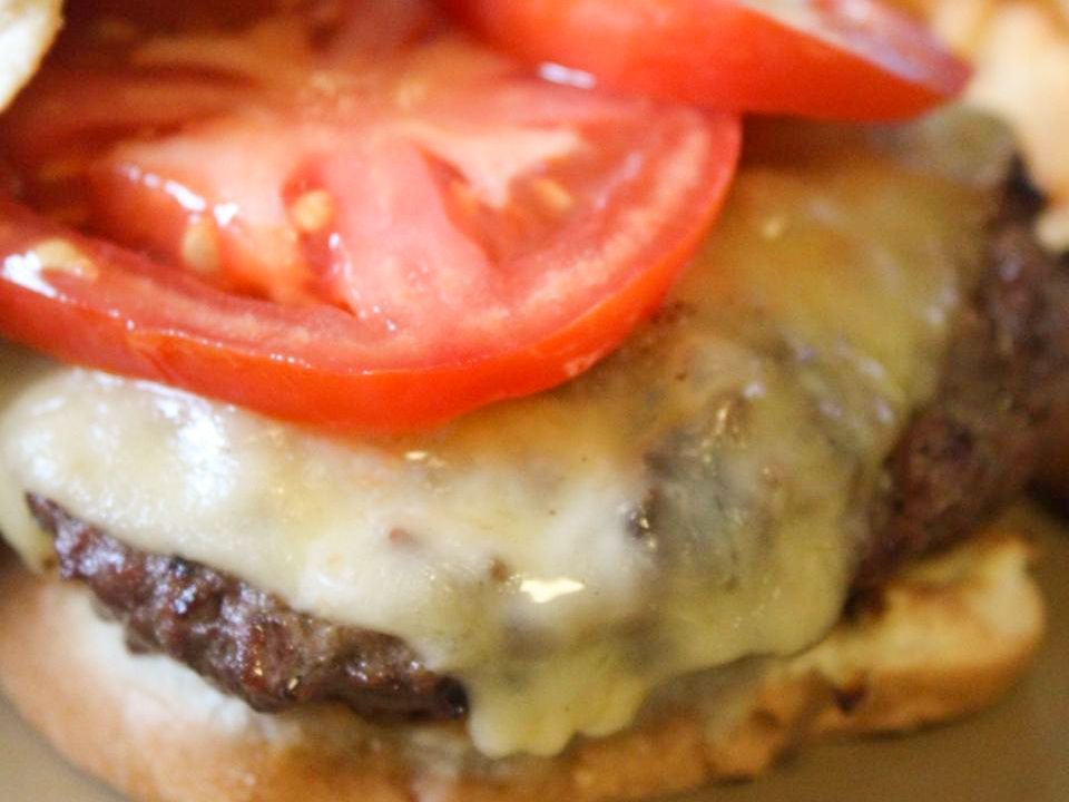 close up view of Bacon, Onion and Cheese Stuffed Burgers with tomato slices on a plate