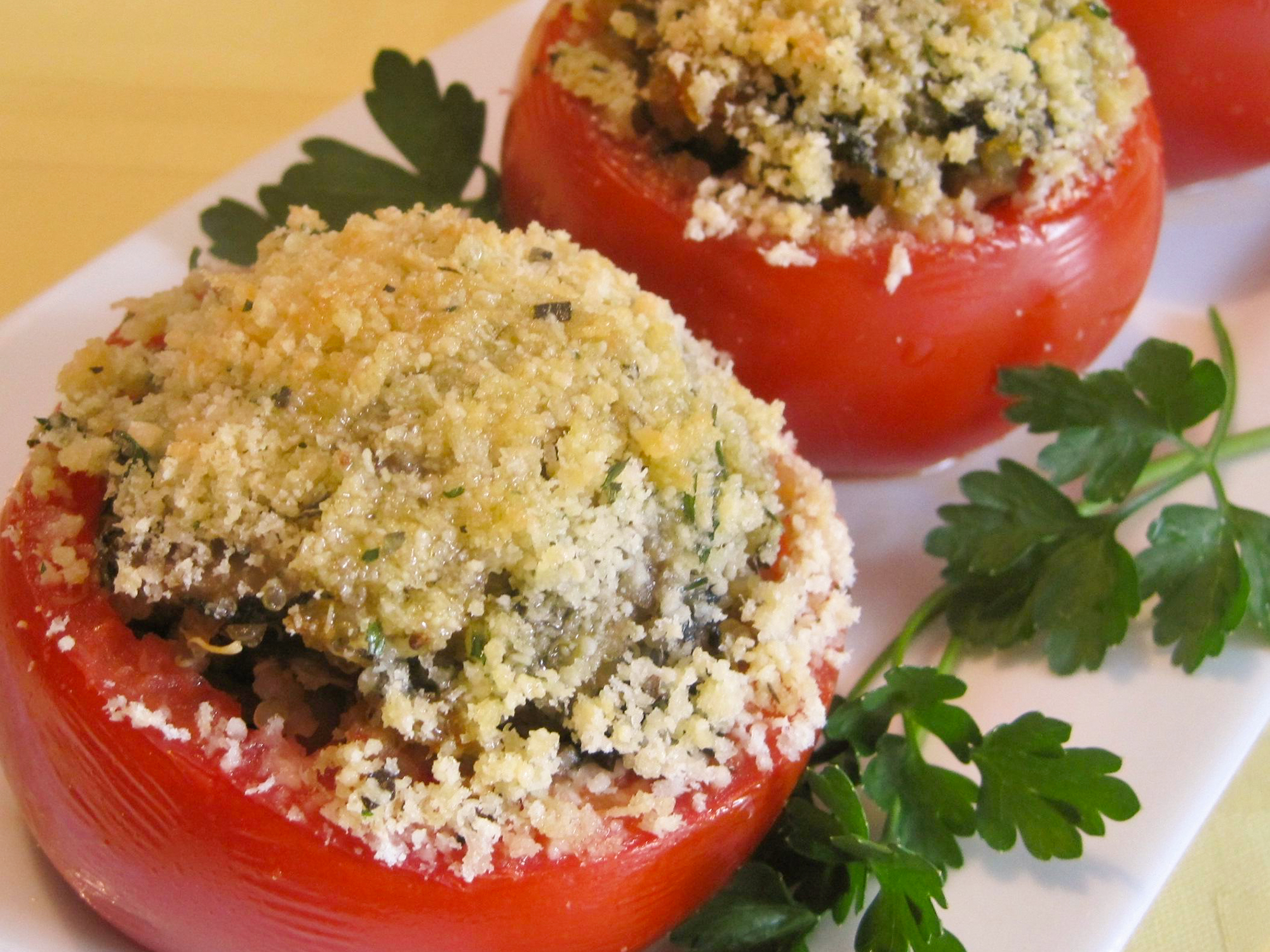 close up view of Baked Stuffed Tomatoes with breadcrumbs on top, garnished with fresh herbs on a white platter