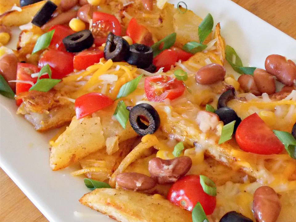 close up view of Potato Nachos with green onions, black olives, beans and tomatoes on a white plate