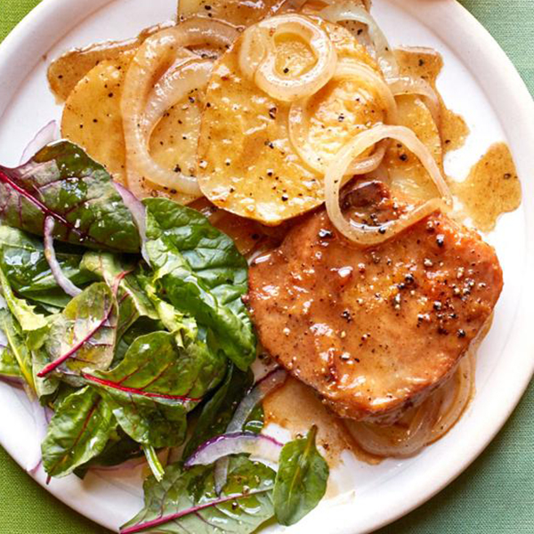 close up view of Skillet Pork Chops with Potatoes and Onion, served with salad on a white plate, served with salad on a white plate