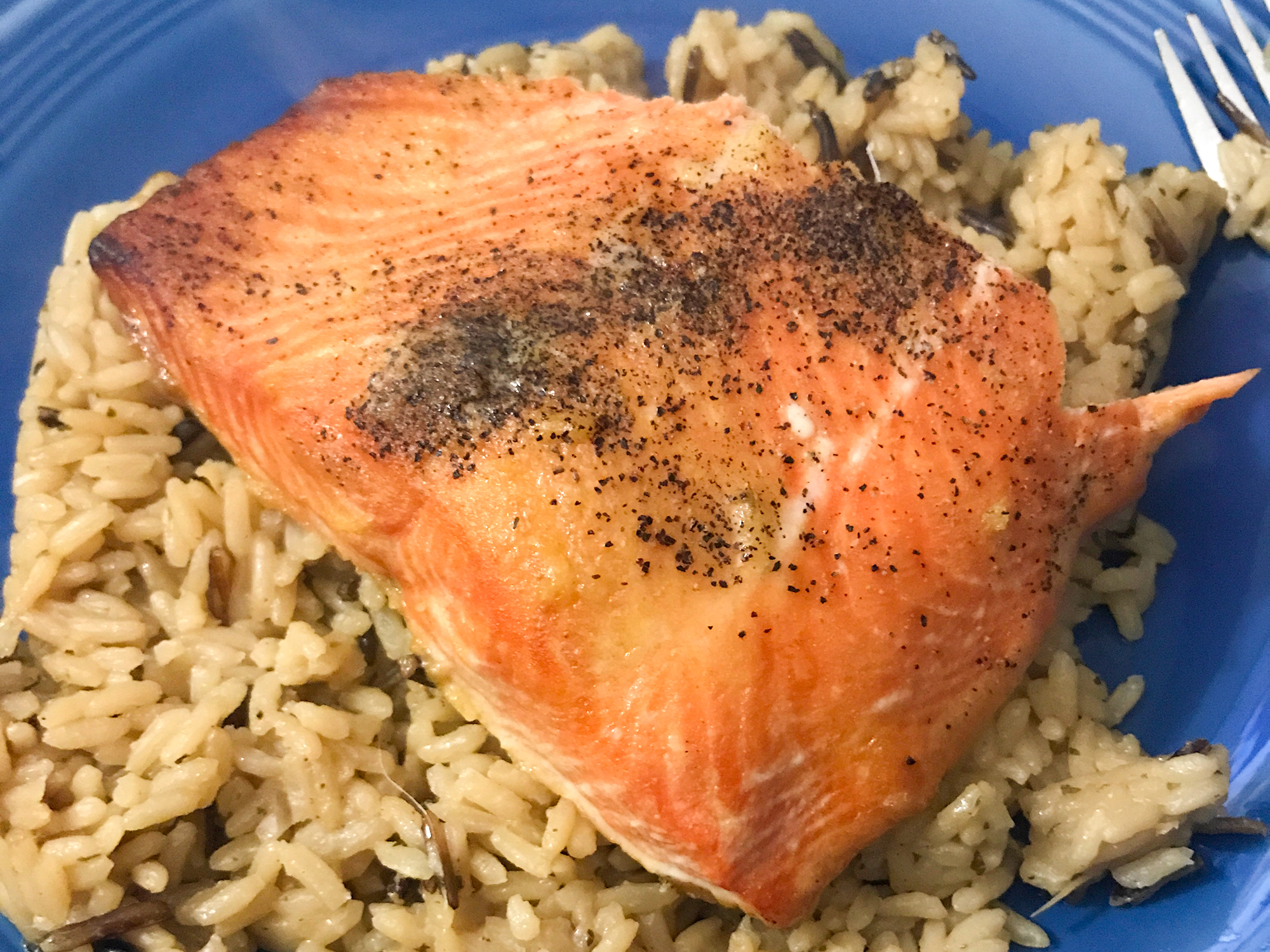 close up view of Ginger Salmon over rice in a blue bowl with a fork