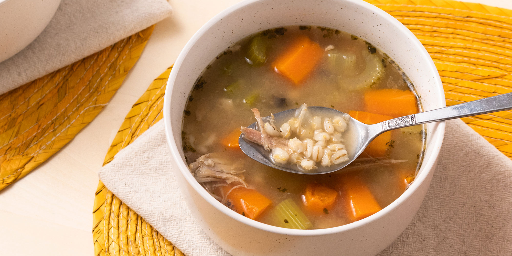 a close up, top down view looking into a bowl of hearty barley soup with a spoon lifting a bite towards viewer