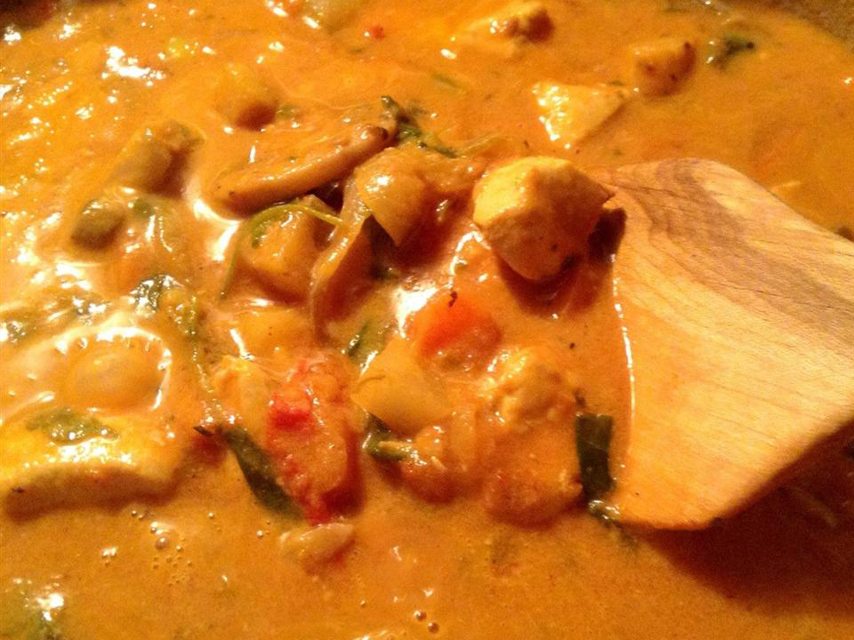 close up view of Coconut Chicken Curry in a bot with a wooden spoon