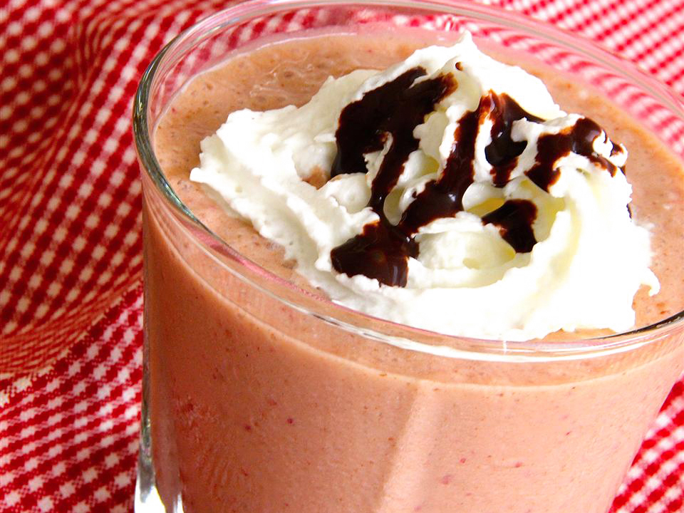 close up view of a Strawberry Banana Nutella Smoothie garnished with whipped cream and strawberry syrup in a glass