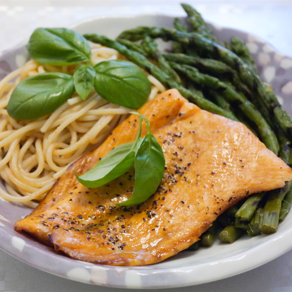 close up view of Lemon-Pepper Salmon garnished with fresh basil, served with spaghetti and asparagus on a plate