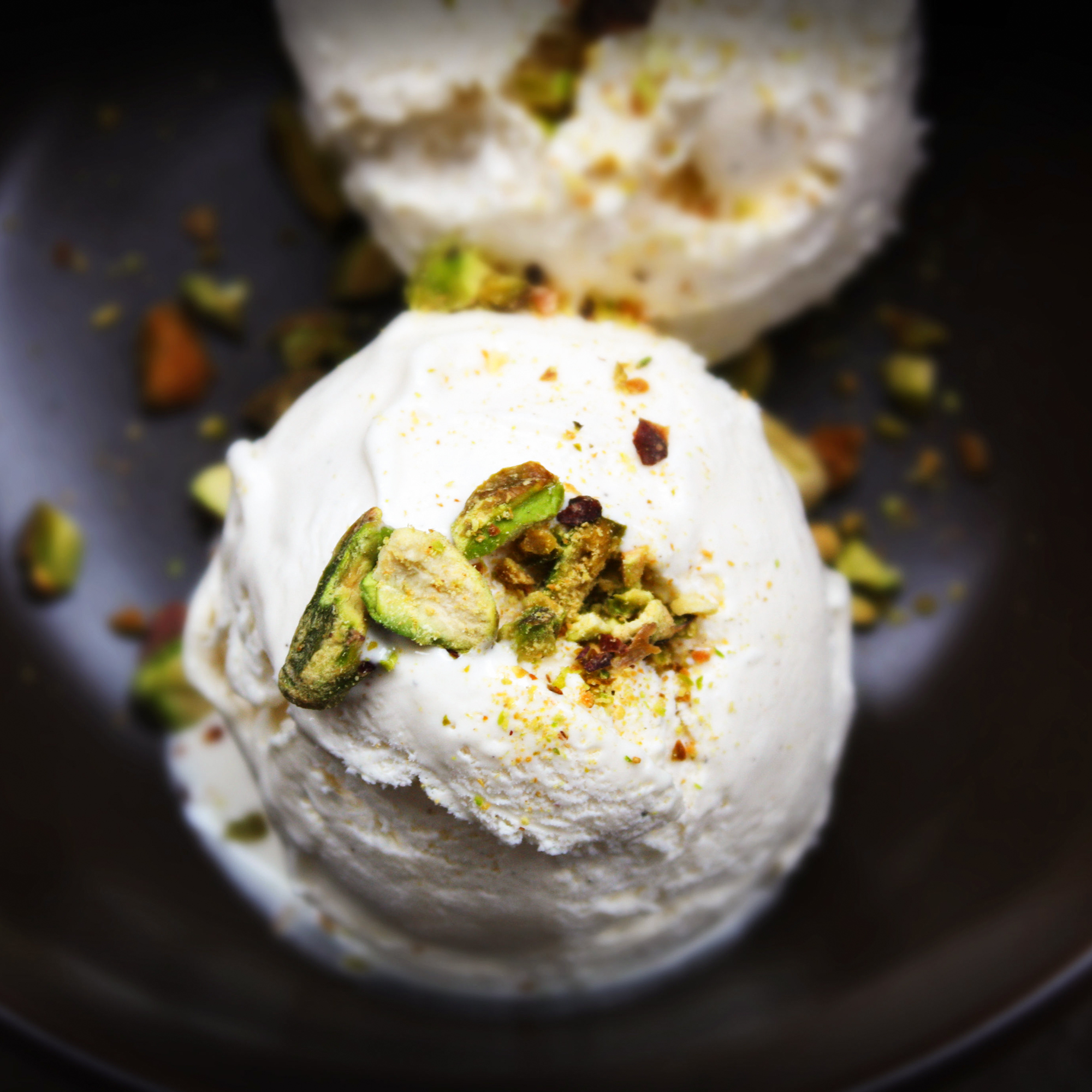 close up view of two scoops of Kulfi ice cream garnished with cardamom in a black bowl