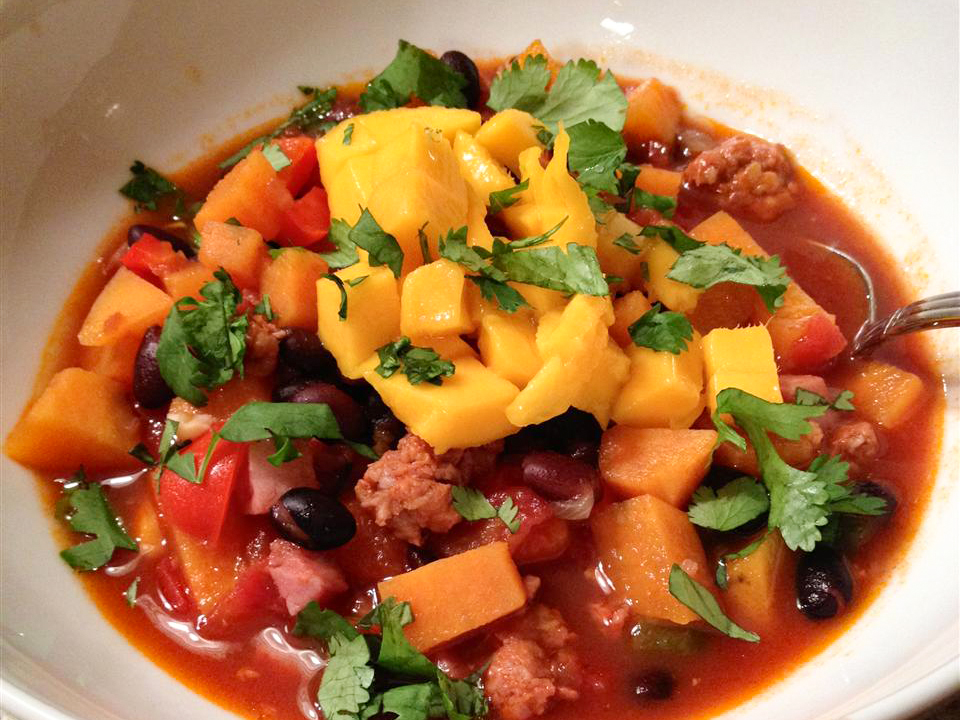 close up view of Brazilian Black Bean Stew garnished with mango and fresh herbs in a bowl