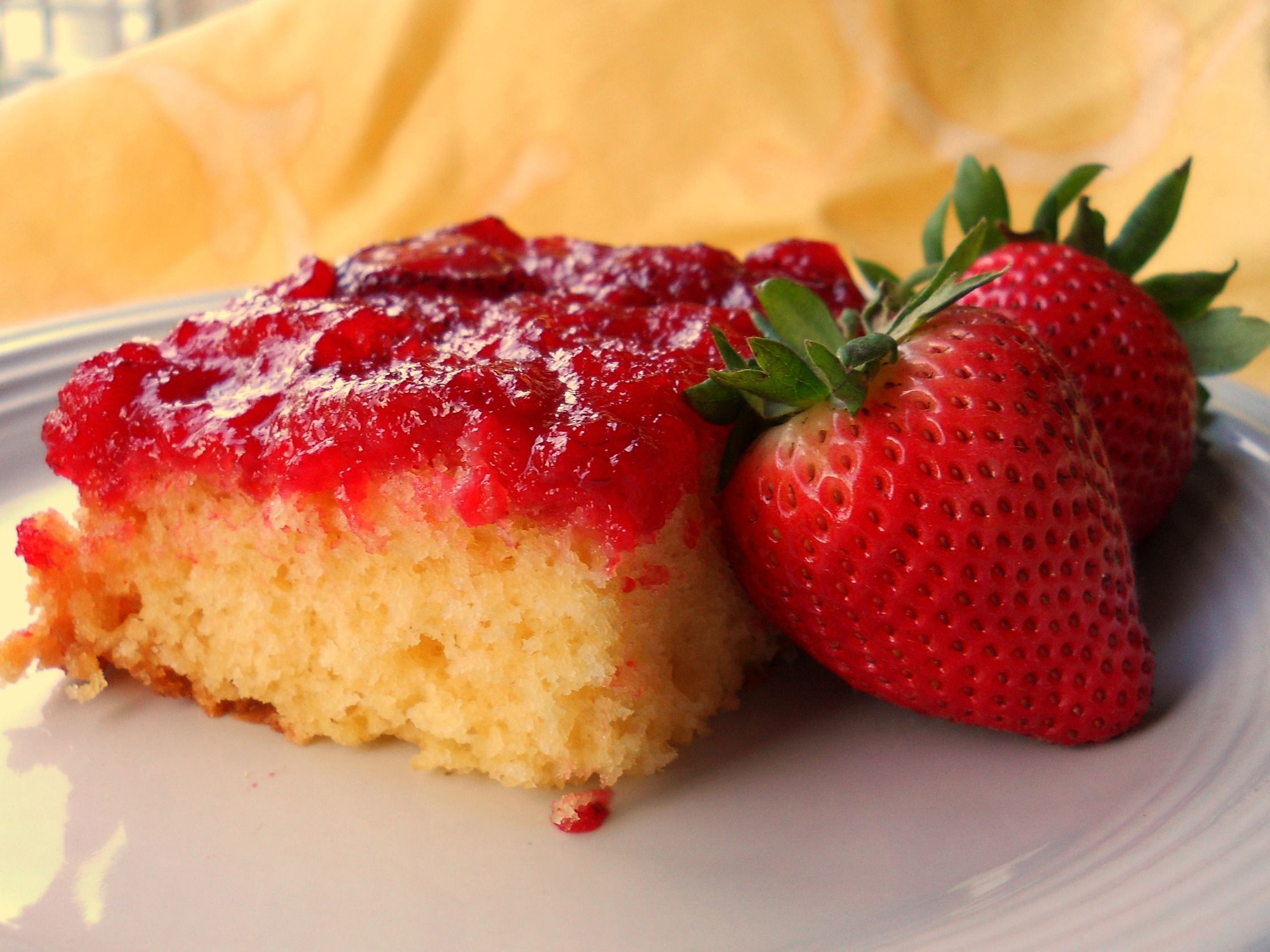 close up view of a slice of Fresh Strawberry Upside Down Cake next to fresh strawberries on a plate