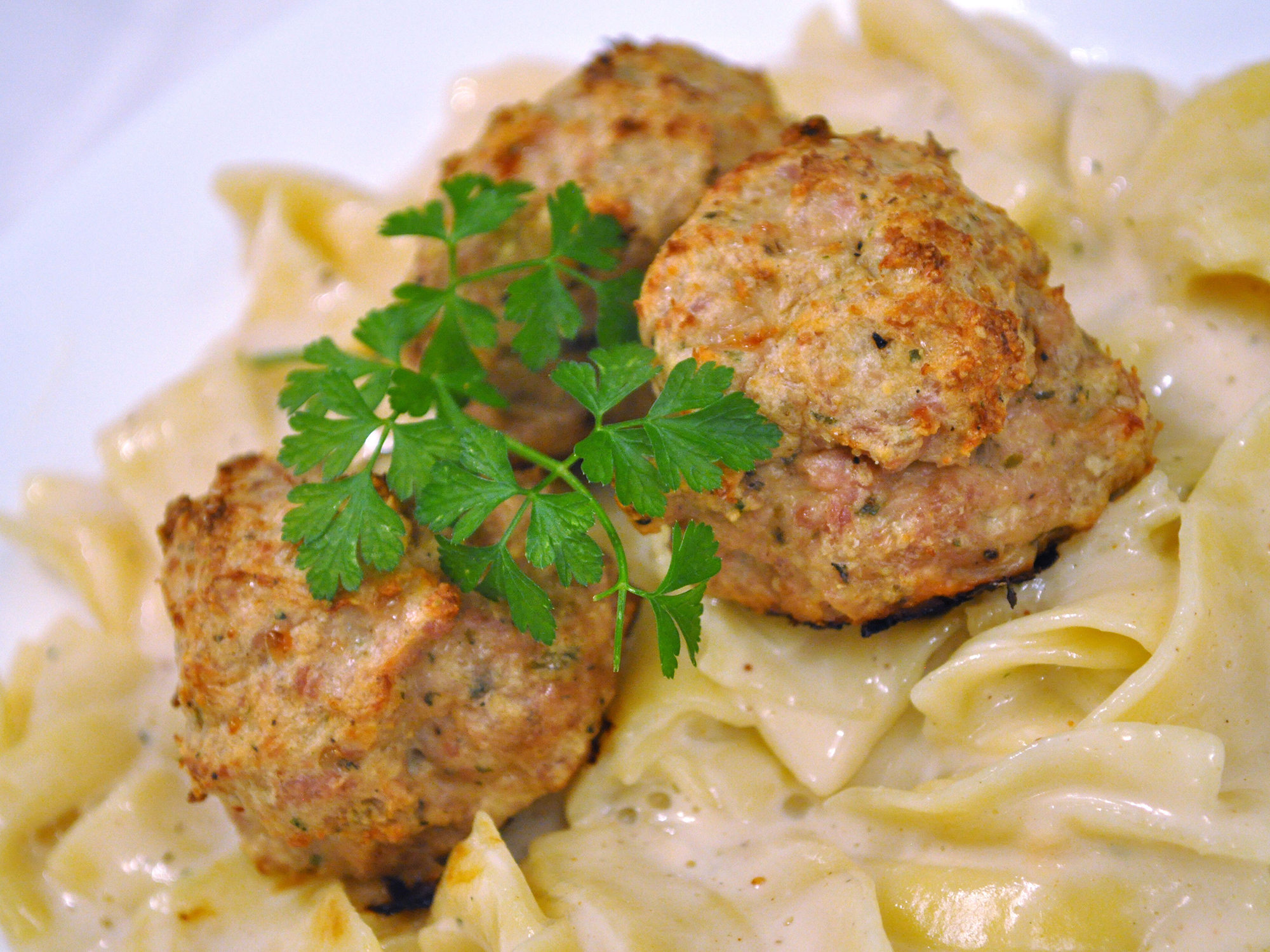 close up view of Cheesy Chicken Meatballs garnished with fresh herbs over pasta on a plate